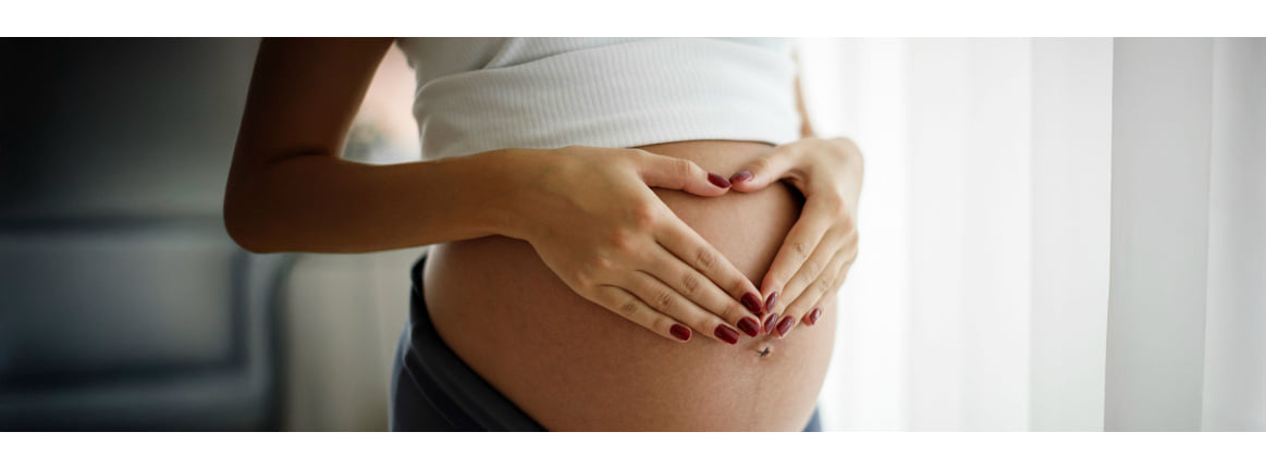 schwangere frau welchen ein Herz mit ihren Handen auf dem nackten Babybauch abbildet