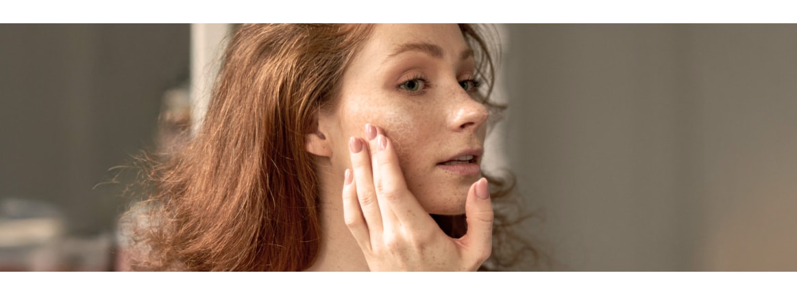 Femme aux cheveux bruns qui se regarde dans le miroir et tient sa main devant son visage