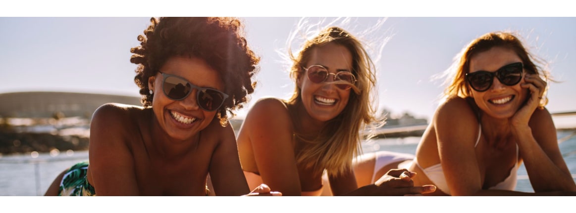 Three women are lying in bikinis on a jetty by the water in the summer sun