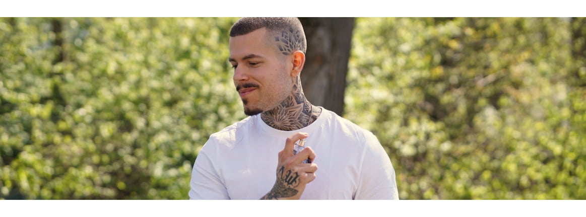 Un homme tatoue se vaporise du parfum sur le cou entre les arbres verts de lete
