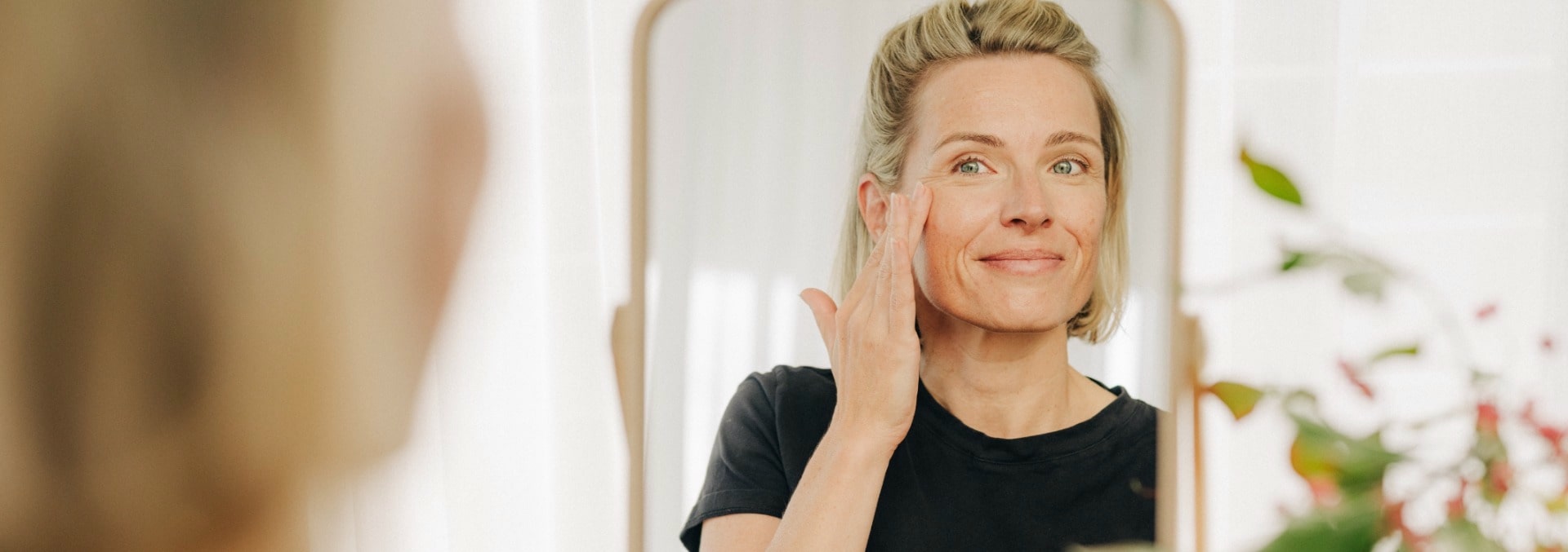 Blonde woman looks at herself in the mirror and dabs cream onto her face with her fingers