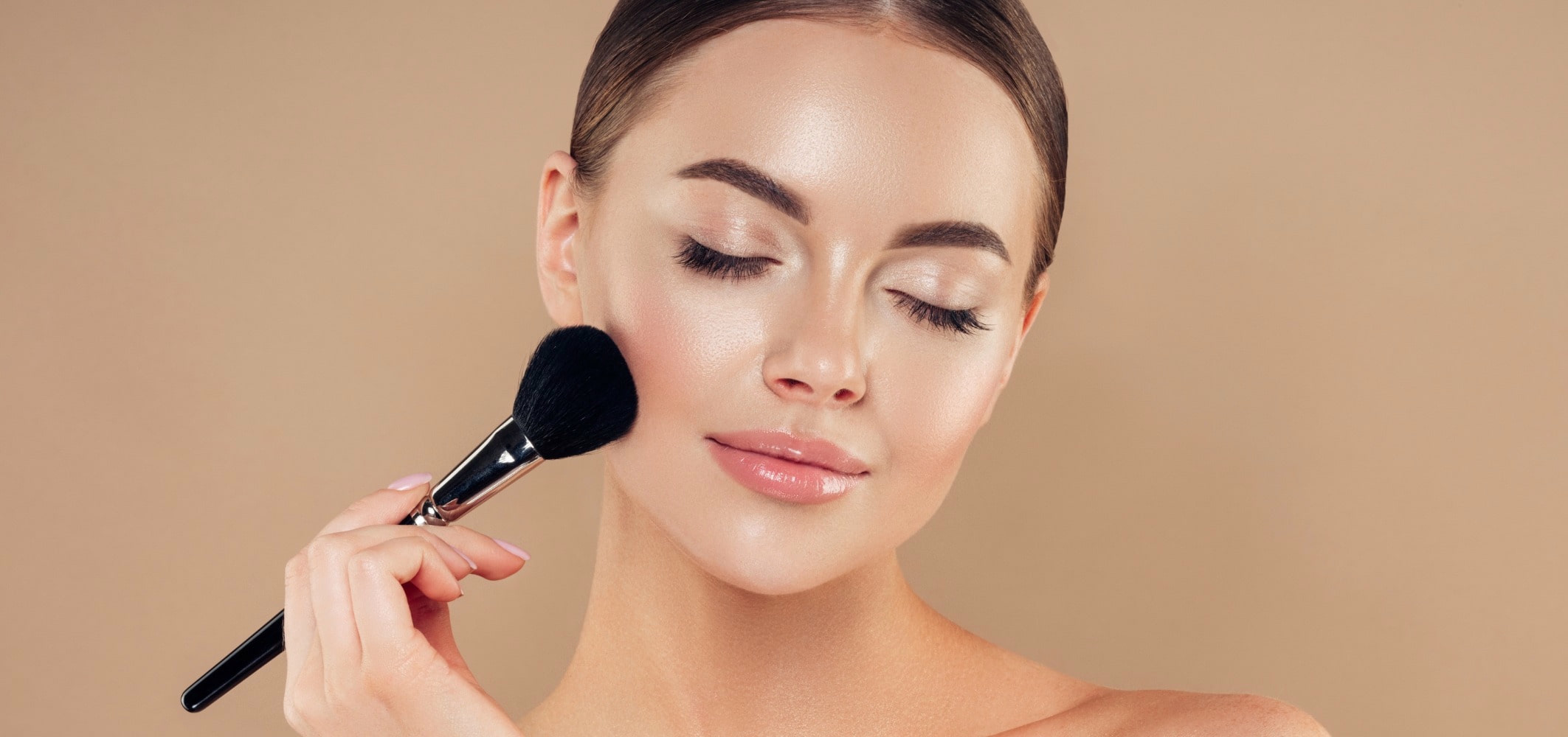 frau mit reiner, glänzenden Haut und geschlossenen Augen, hält sich Make-Up Pinsel ins Gesicht
