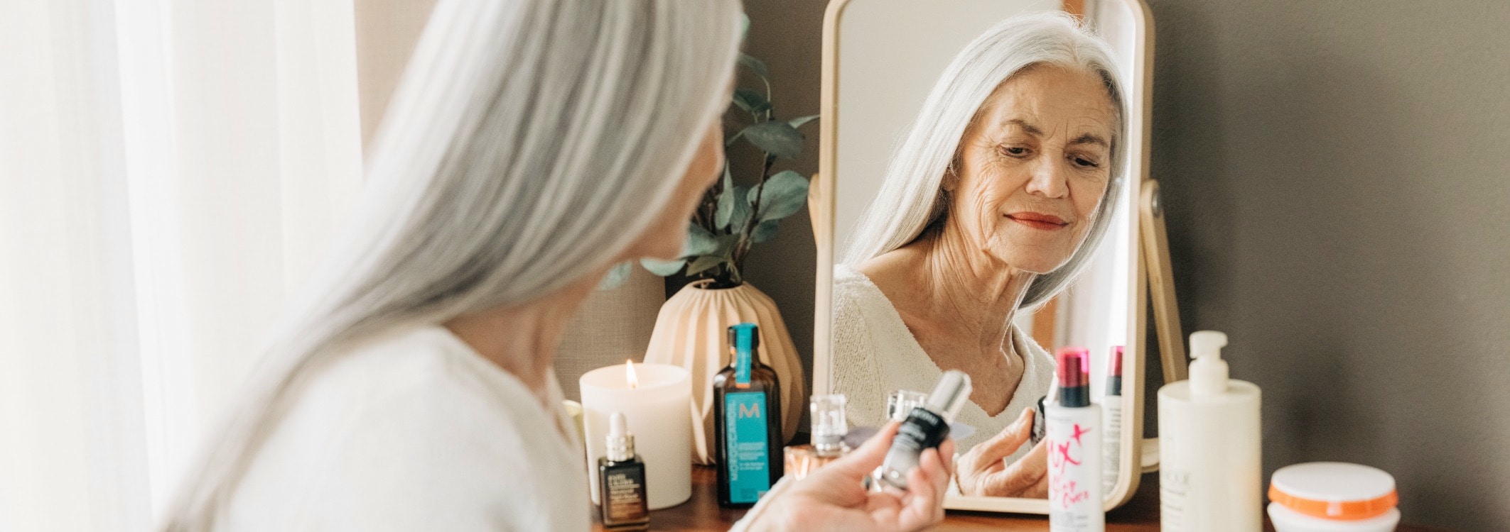 ältere dame sitzt vor kleinem spiegel und betrachtet beauty produkte