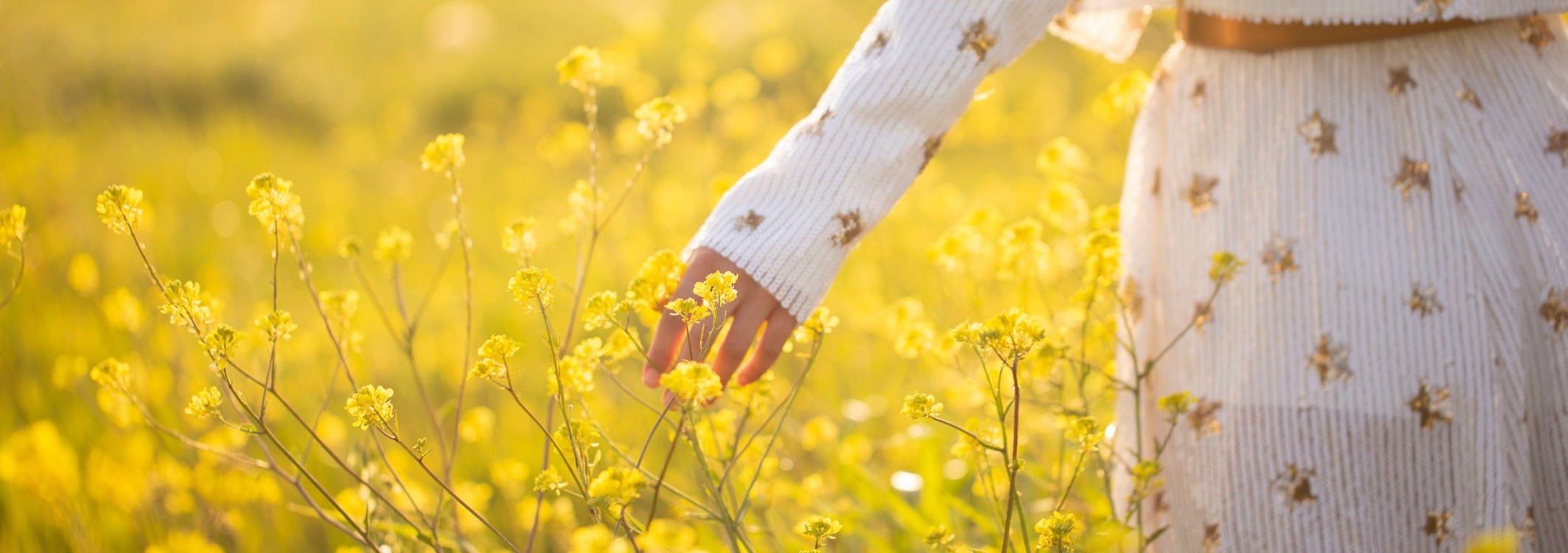 Une femme vetue dune robe blanche traverse une prairie couverte de fleurs jaunes