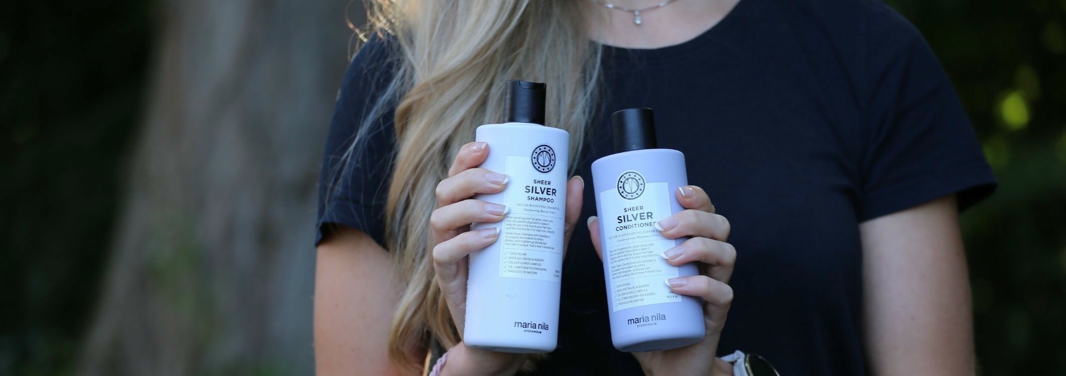 Des mains feminines tiennent devant la caméra le shampooing et l\'après-shampooing argentes de la marque Maria Nila