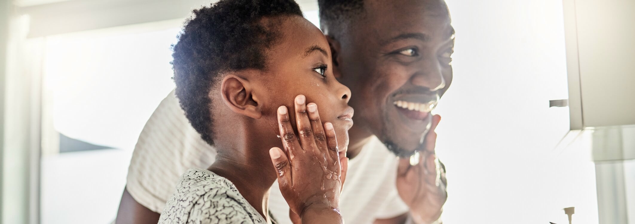 Un homme se tient devant le miroir avec son fils et ils se lavent le visage ensemble