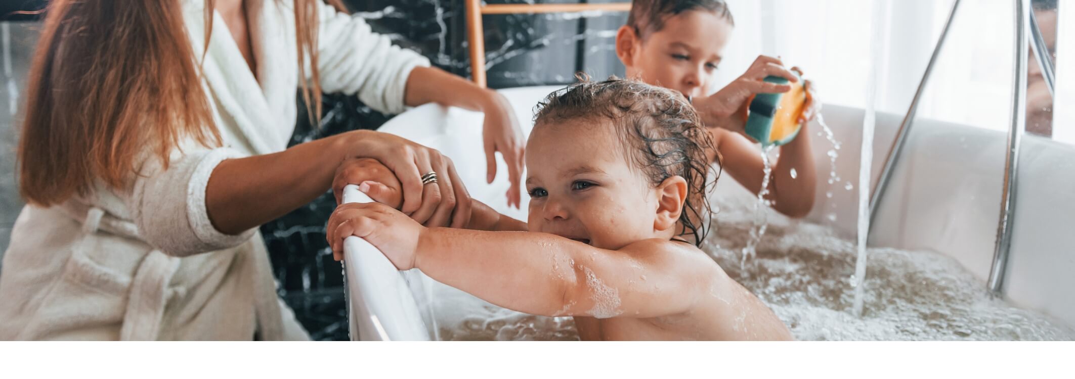 Des bebes jouent dans la baignoire avec une eponge et de la mousse