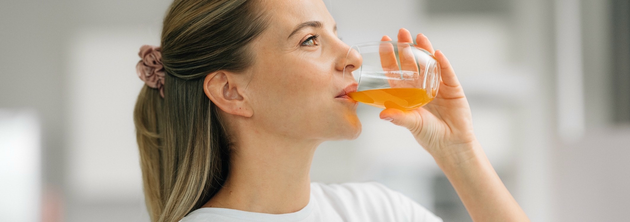 Jeune femme blonde buvant un liquide orange dans un verre